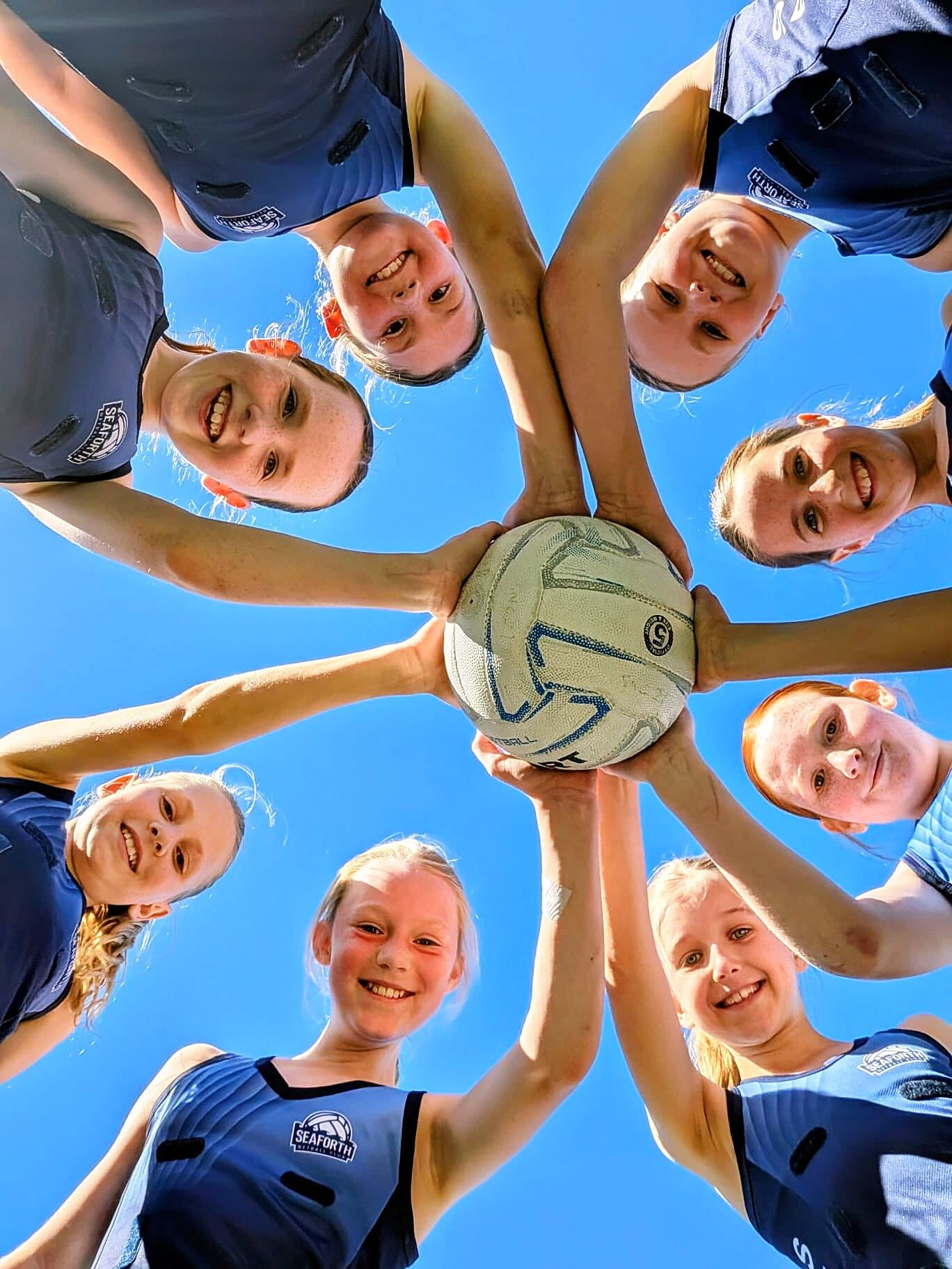 Seaforth Netball team huddle with hands on the ball under a blue sky